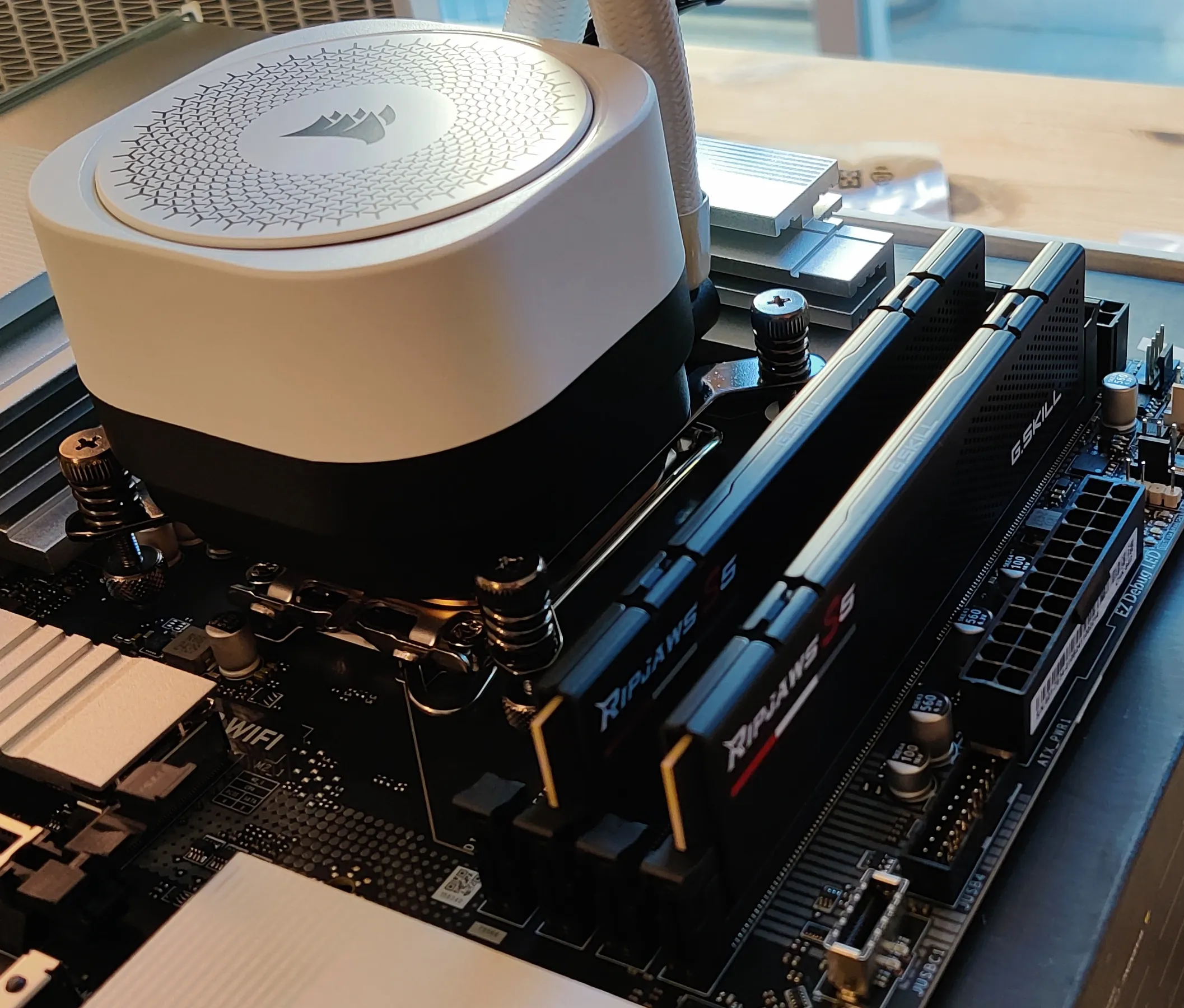 Two black RAM sticks slotted into a motherboard next to a white all-in-one cooler