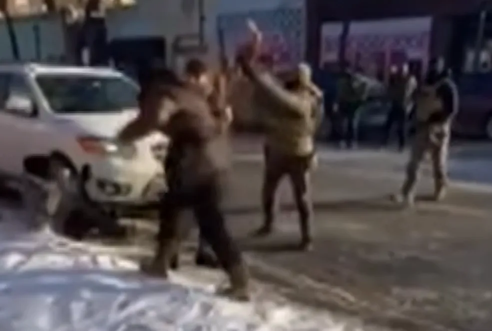 Grainy freeze frame shows Alex Pretti raises one hand and holds his phone in another. He looks at a woman who's been shoved to the ground. One agent is making physical contact with Pretti. Another is looking at the woman. A third is approaching.